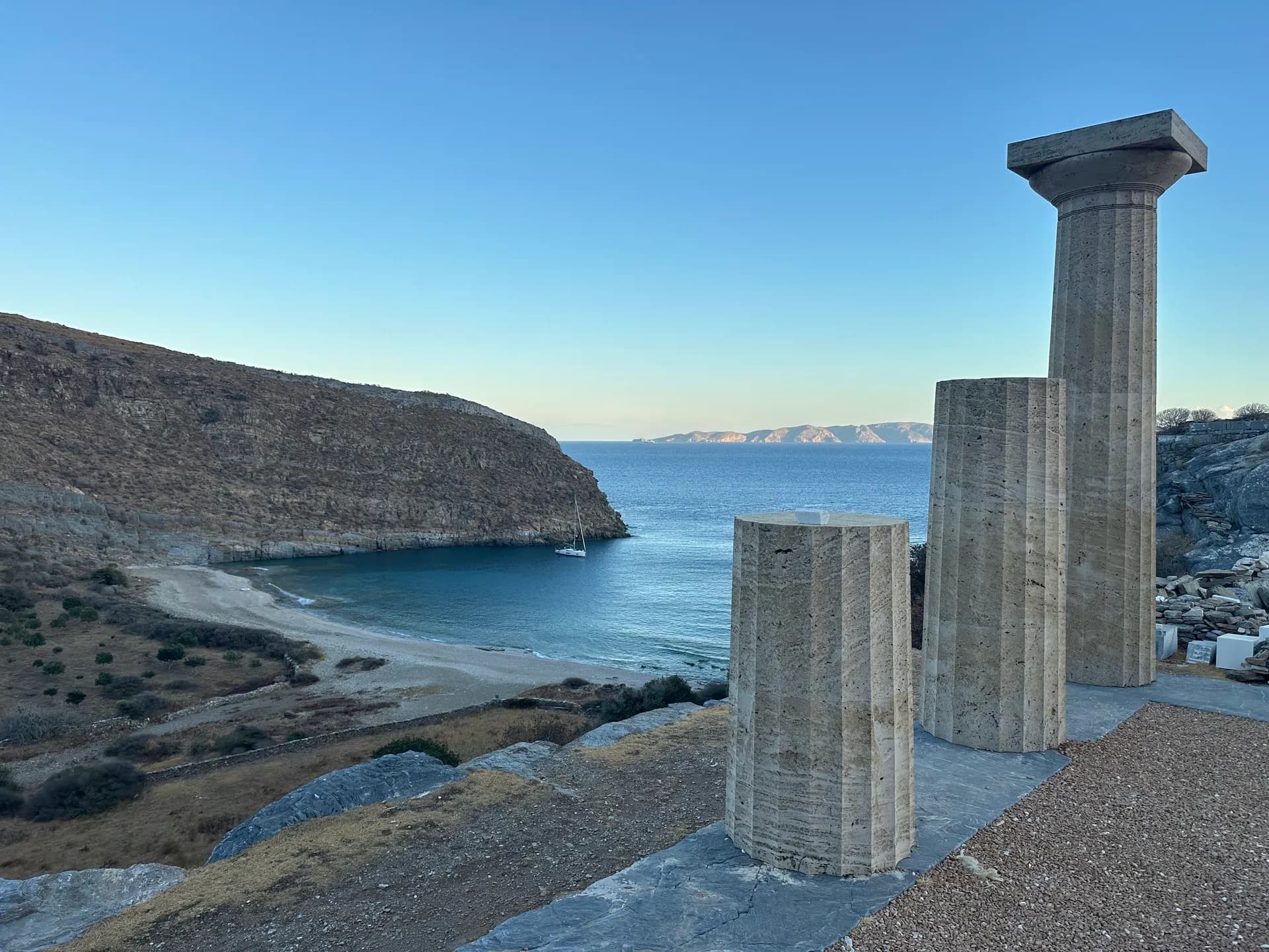 Ancient stone columns overlooking a quiet bay with a lone sailboat